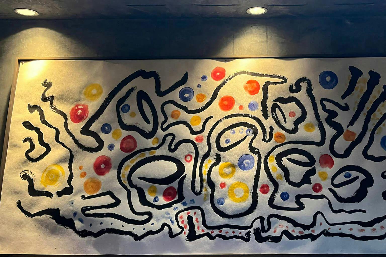 At the center of the painting by artist Moto are the outlines of a sake carafe and sake cups. The colorful dots correspond to sake types on the drink menu: Yellow for junmai, blue for nigori, orange for ginjo and red for daiginjo. | Photo by Taylor Markarian.