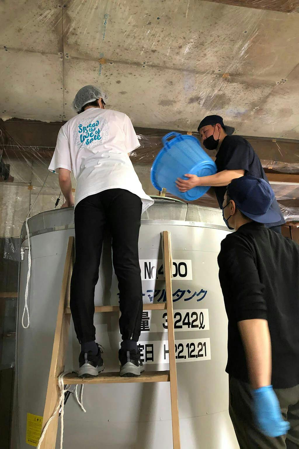 Rina and Azusa work with the Mitsutake brewing staff to add rice to the fermentation tank. | Photo by Azusa K.