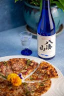 Hakkaisan “Tokubetsu Junmai”, with a clear glass cup with blue mini stem, served with pizza