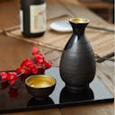 “Mino no Takumi” Black Sakazuki Cup With Blue Drip Glaze and Gold Interior, on a table