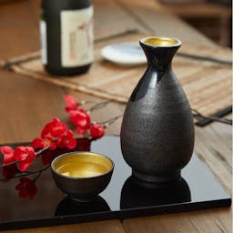“Mino no Takumi” Black With Blue Drip Glaze and Gold Interior Sake Set, on a table